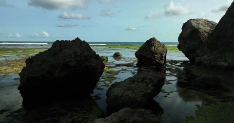 Rocks on sandy beach by ocean, under sky with water horizon Video stock 270561734