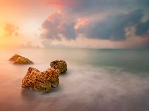 Rocks in sea over dramatic sky during sunrise Stock Photos