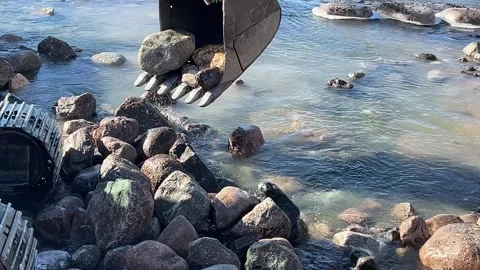 Rocks splash out of backhoe bucket at river construction site Video stock 273176396