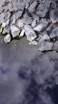 Rocks by the water with sky reflected in it Foto stock