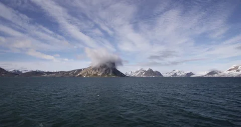 Rocky arctic mountain range across sea with one gray cloud over peak Stock Footage 62013215