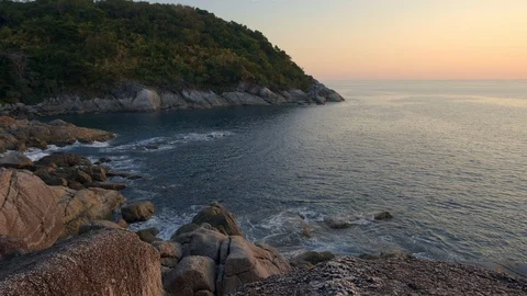 Rocky beach with big sharp stones, hill and forest in warm sunset Stockbeeldmateriaal 114917706
