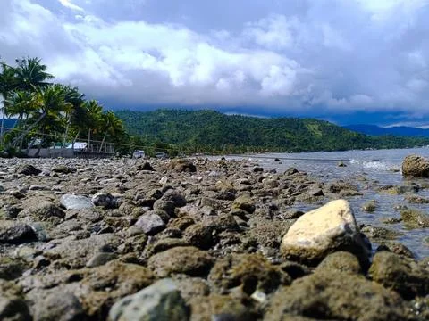 Rocky Beach with Mountain and Clouds Background Stock Photos