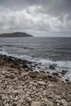 Rocky beach with waves breaking on overcast day Stock Photos
