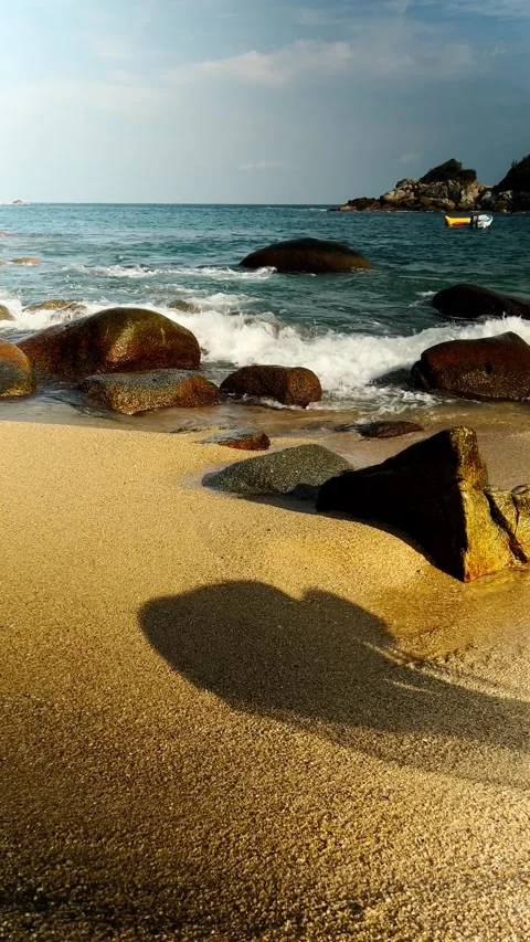 Rocky beach with waves washing over sandy shore and long human shadow under Stock Footage 343711573