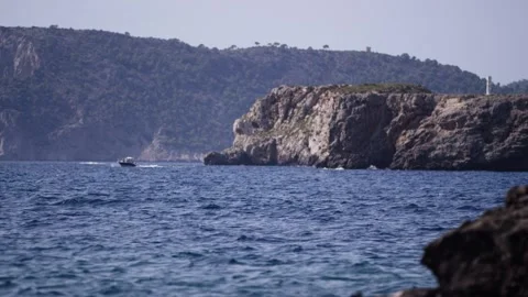 Rocky cape and cliffs over deep blue sea, small motorboat passing by 動画素材 341580708