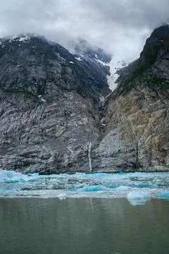 Rocky cliffs with low clouds and ice from Dawes Glacier Stock Photos