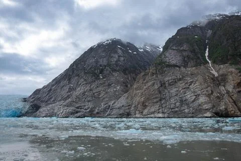 Rocky cliffs with low clouds and ice from Dawes Glacier Stock Photos
