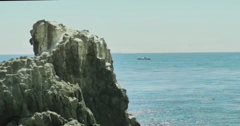 Rocky Cliffs Overlooking a Calm Sea with Distant Boat 스톡 동영상 323571815