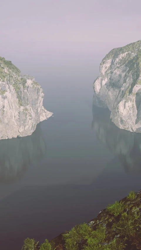 Rocky cliffs rise from calm waters at daybreak near a quiet coastline Stock Footage 327266597