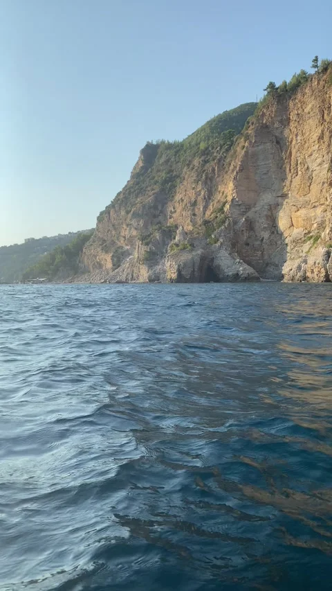 Rocky coastal cliffs rise steeply above the blue sea as viewed from a boat Vídeos de archivo 343790903