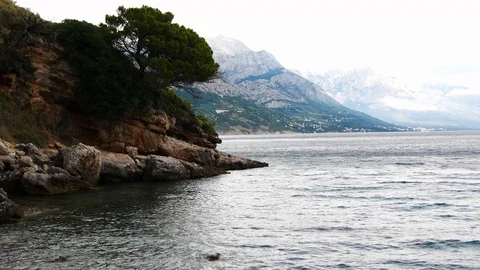 Rocky coastline lined with pine trees, wind at sea, waves Stock Footage 95484093