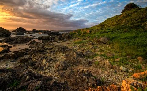 Rocky Coastline at Sunset with Dramatic Sky and Green Hillside Stock Photos