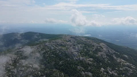 Rocky granite summit of Mount Monadnock rises above wisps of cloud, forested Stock Footage 345699421