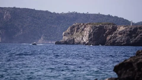 Rocky Headland and Cliffs above Deep Blue Sea, Passing Motorboat, Wide Shot Stock Footage 340626726