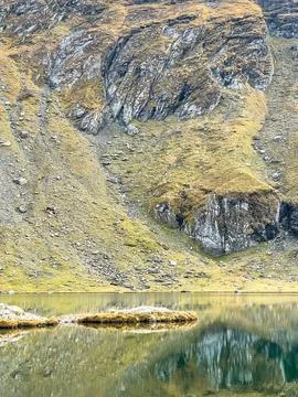 Rocky mountain slopes reflected in Balea Lake in the Fagaras Mountains, Romania Stock Photos