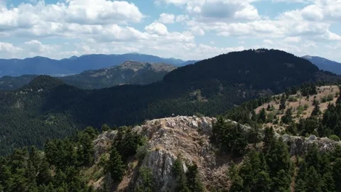 Rocky mountain summit with climbers above dense forested slopes and ranges Stock Footage 344093818