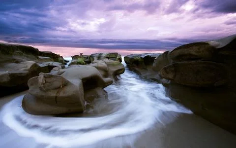 Rocky Ocean Coast at Sunset with Dramatic Purple Sky Stock Photos