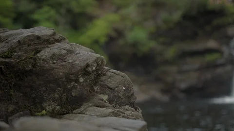 Rocky riverside with waterfall blurred in background. Video stock 113159343