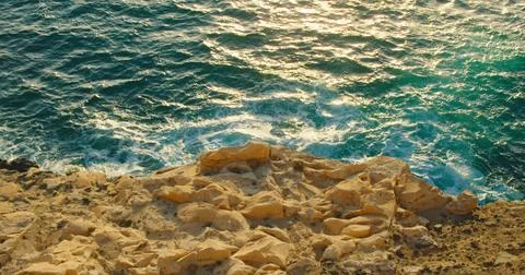 Rocky sandstone coast with ocean waves splashing on limestones at sunset. Water Stock Photos