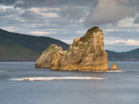 Rocky sea stack at a tranquil Basque coastline - A long exposure of a large.. Stock Photos