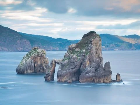 Rocky sea stack at a tranquil Basque coastline - A long exposure of a large.. Stock Photos