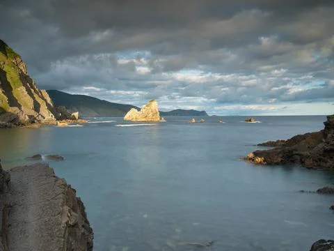 Rocky sea stack at a tranquil Basque coastline - A long exposure of a large.. Stock Photos