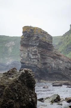 Rocky sea stack on the wild coast under cloudy sky, rugged coastal landscape Stock Photos