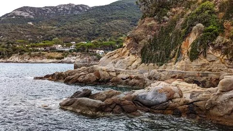 Rocky seaside cliffs with coastal path and houses surrounded by green hills. Stock Photos