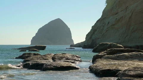 Rocky shoreline with a massive sea stack rising from the ocean under a clear -80 Stock Footage 345519810