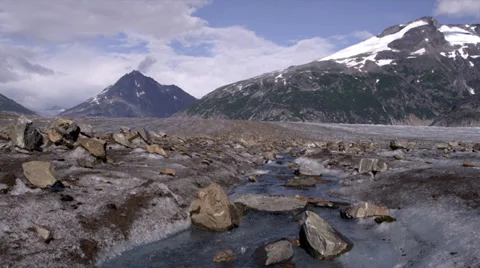A rocky stream flows toward camera with snow capped mountains in background in Stock Footage 36311998