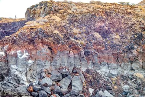 Rocky wall of volcanic lava with arid brown wild vegetation on top Stock Photos