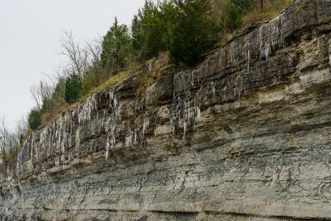Rocky winter cliff with dramatic sedimentary rock layers covered in icicles Foto stock