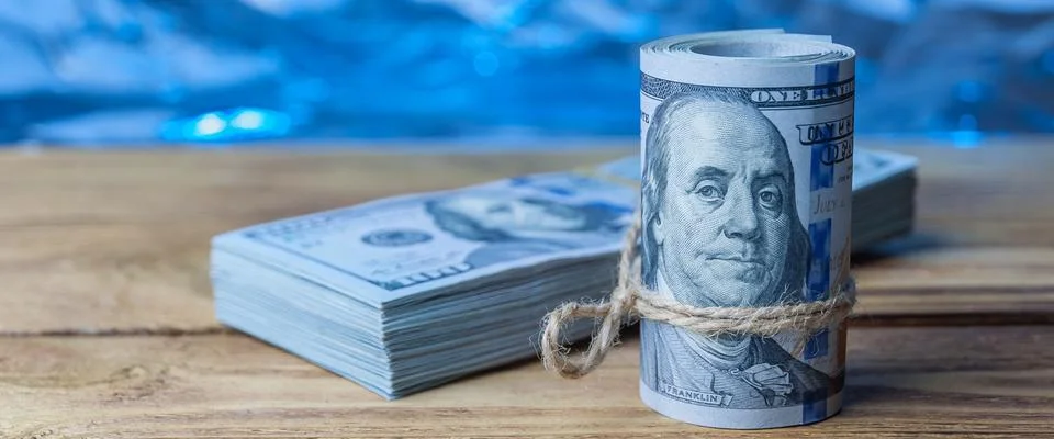 A roll and a bundle of one hundred dollar bills on a wooden table. Stock Photos