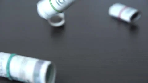 A roll of banknotes one by one falls on the brown table top. Vídeo Stock 240560373
