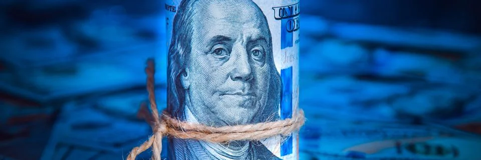 A roll of dollars on the background of scattered hundred dollar bills in blue Stock Photos