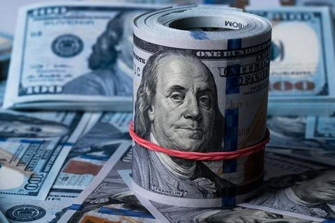 A roll of dollars on the background of scattered one hundred dollar bills. Stock Photos