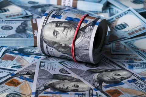 A roll of dollars on the background of scattered one hundred dollar bills. Stock Photos