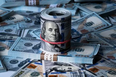 A roll of dollars on the background of scattered one hundred dollar bills. Stock Photos