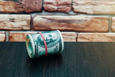 A roll of dollars bill. Close-up, against a brick wall of dark red brown colo Stock Photos