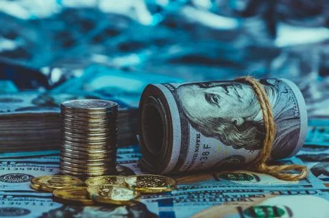 A roll of dollars with coins on the background of scattered one hundred dolla Stock Photos