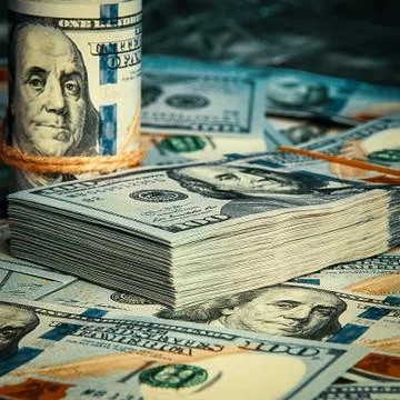 A roll of dollars with coins on the background of scattered one hundred dolla Stock Photos