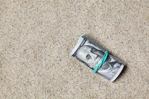 Roll of dollars lost in the sand. Left on the beach Stock Photos