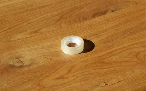 Roll of plastic sellotape lying on plain solid wood table Stock Photos