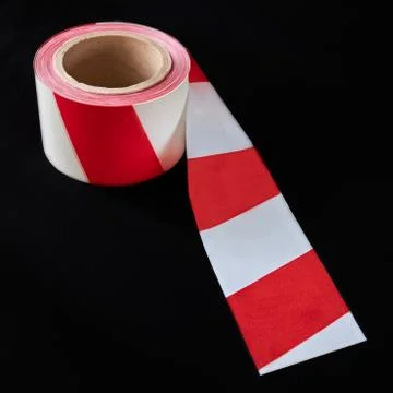 Roll of red and white caution tape against a dark background Stock Photos