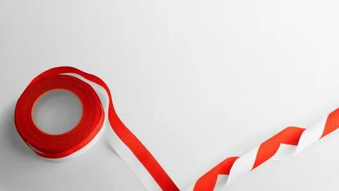 A roll of red and white warning hazard tape unrolling on a plain white surf.. Stock Photos