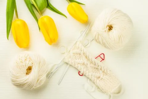 Roll of white soft knitting yarn, knitting mittens and yellow tulips Stock Photos