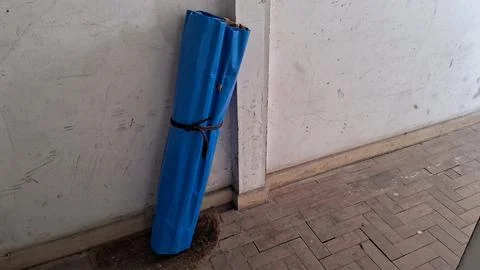 Rolled blue plastic mat leaning against a weathered interior white wall Stock Photos