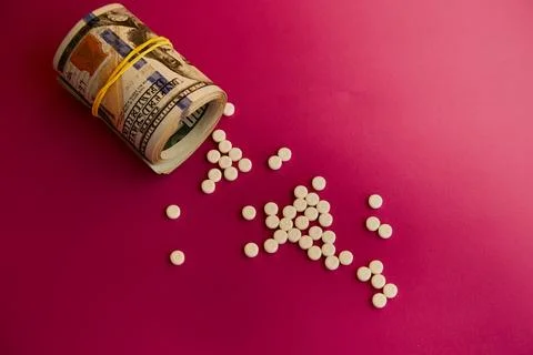 Rolled bundle of hundred-dollar bills with white pills spilling out, money fo Stock Photos
