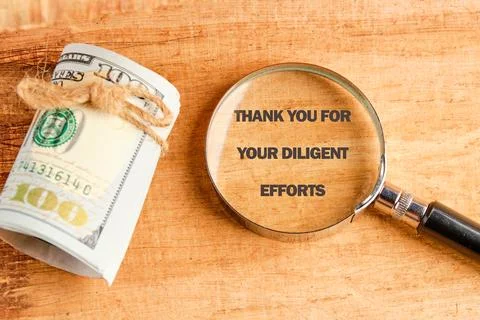 A rolled bundle of money is placed next to a magnifying glass highlighting a  Stock Photos